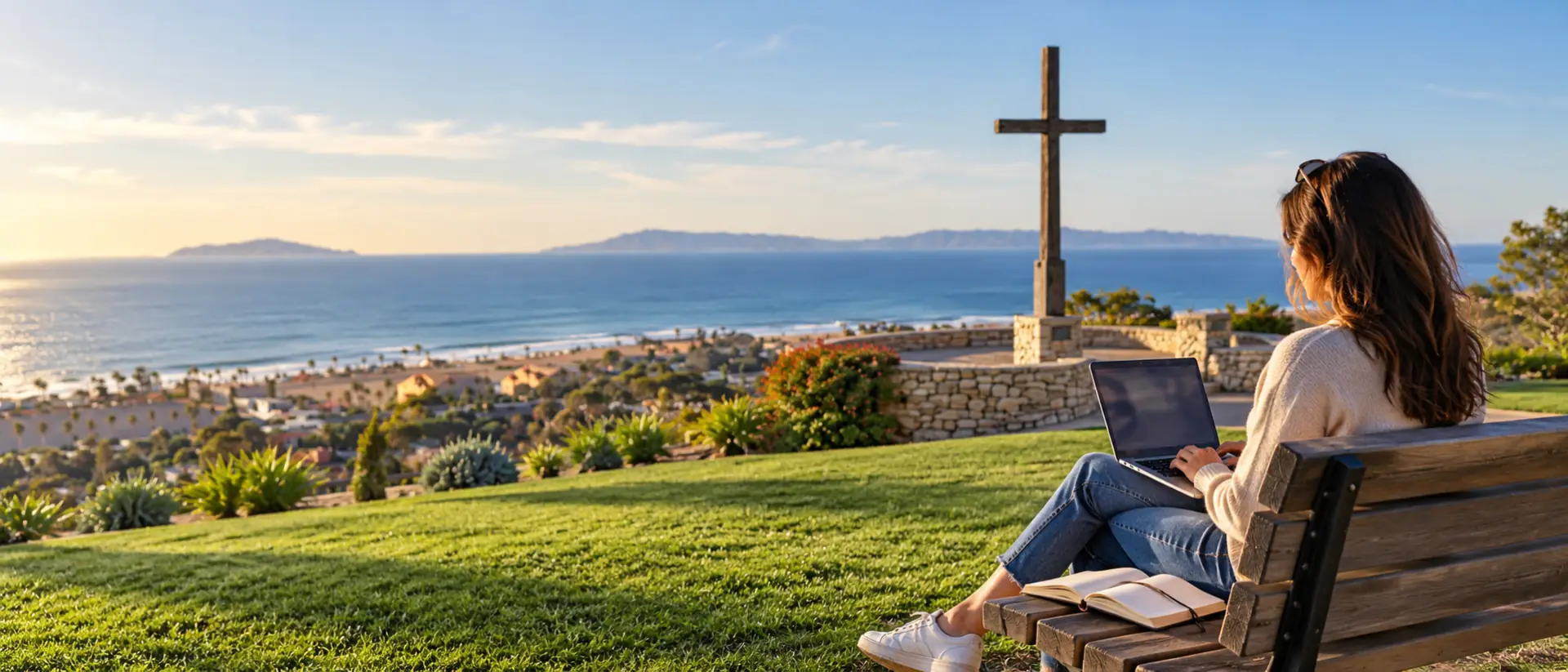 Writer working on a laptop on a bench on the Serra Cross hilltop with the ocean and Channel Islands behind